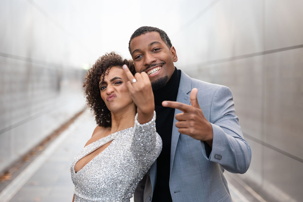 engaged couple posing for a photo. Woman is holding up ring finger.
